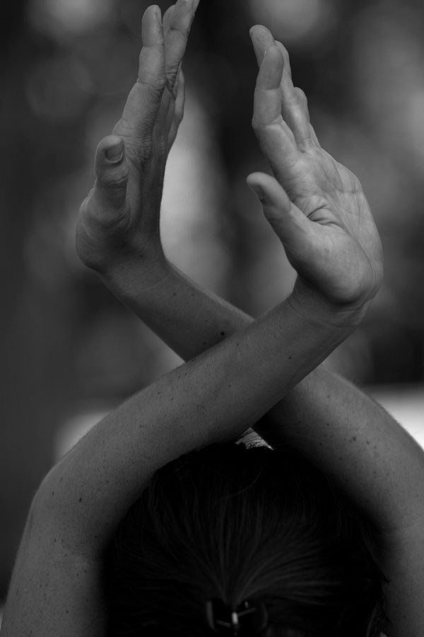 Two hands pressed together overhead with forearms crossed, in black and white